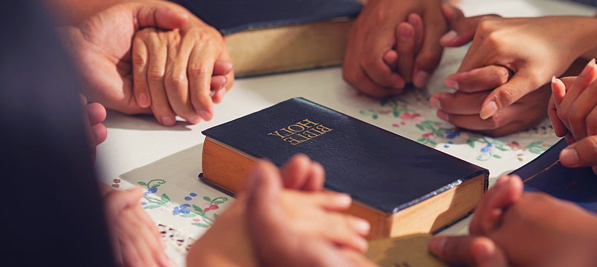 people holding hands with the bible at the center
