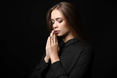 Beautiful young woman praying on dark background