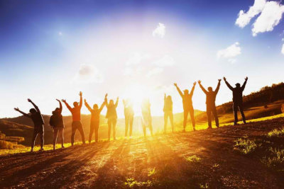 Big group of happy friends stands on sunset backdrop with raised arms together